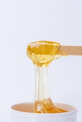 Liquid yellow sugar paste or wax for depilation on a wooden stick close-up on a white background