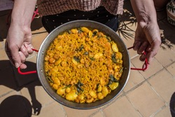 A delicious Paella, traditional rice dish from Valencia in Spain. Paellera, cooking pot and dish from Valencia held by the cook.