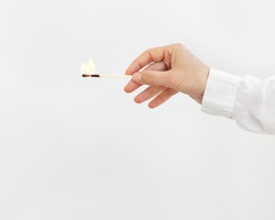 Female hand holds lit match on light background. Wooden matchstick with fire. Fire Hazard concept.
