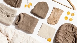 Autumn warm clothing beige colored, folded knitted wear, hat, scarf, gloves, sweater with craft paper for copy space. Flat lay from female fashion autumnal outerwear for cold weather in fall season.