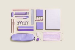 School stationery very peri trend color, pencils, pens, paper clips, pencil case, medical mask. Back to school flat lay square composition on beige. Office supplies new normal on table, top view
