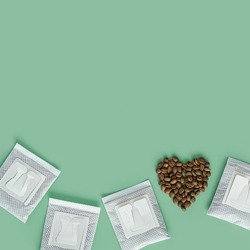 Drip coffee bag and heart from coffee beans, ground coffee for brewing in cup, pack with paper bag drip coffee filter, mint color background, top view, minimal flat lay with copyspace, pastel color