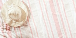 Minimal summer beach concept top view wide-brimmed sun hat at sunlight on striped beach towel, pastel pink color background, copy space, palm leaf shadow. Lifestyle fashion pale pink flat lay, banner