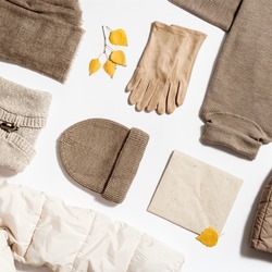 Autumn warm clothing beige colored, folded knitted wear, hat, scarf, gloves, sweater with craft paper for copy space. Creative Flat lay from female fashion autumnal outerwear for cold weather in fall