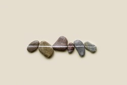 Aesthetic minimal flat lay sea pebble stones with white line, beige background. Composition from natural colored stone on the same level. Balance or harmony concept, top view, horizontal row rocks.