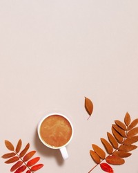 Cup of coffee with milk and red autumn leaves on pastel pink paper background. Autumn, fall composition, monohrome flat lay, top view, copy space.