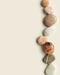 Aesthetic minimal flat lay with sea pebble stones on beige background with copy space. Row from natural smooth stone pastel color and sardonyx gemstone. Summer concept, top view, empty space