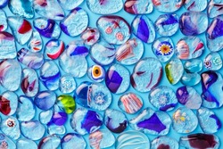 Collection of colorful glass beads of different sizes and shapes. Colored Venetian, Murano glass, millefiori. On a blue background. Flat lay, top view