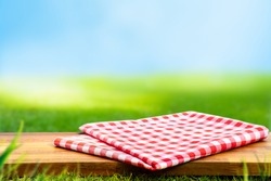 Red checked tablecloth on wood with blur green courtyard background.Summer and picnic concepts.Design for key visual food and drink products.no people