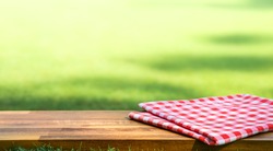Red checked tablecloth on wood with blur green courtyard background.Summer and picnic concepts.Design for key visual food and drink products.no people