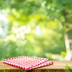 Red checked tablecloth on wood with blur green bokeh of tree background.Summer and picnic concepts.Design for key visual food and drink products.no people