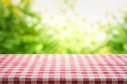 Red checkered tablecloth texture top view with abstract green bokeh from garden in morning background.For montage product display or design key visual layout.