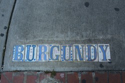 vintage ceramic tiles embedded into concrete street corner spell out BURGUNDY with contemporary graffiti details of stars and the world love in gold marker on French Quarter New Orleans street