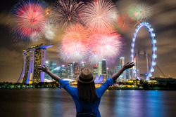 Young woman traveler celebrate and looking view of Singapore city landmark financial district at twilight sunset scene with multicolor firework celebration. Singapore city in national day celebration.