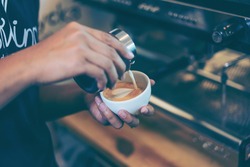 Barista using coffee machine preparing fresh coffee or latte art and pouring into white cup at coffee shop and restaurant, bar or pub. 