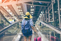 Young woman traveler in international airport with backpack holding suitcase or baggage in her hand, Beautiful young tourist girl with backpack and carry on luggage in airport terminal, on travelator