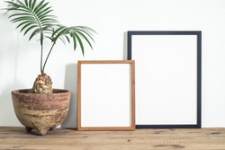 Black and wooden brown frame poster with beautiful houseplant on wooden table. Home decoration