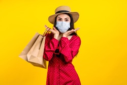 Portrait of young happy carefree asian woman wear hat and facemask carrying shop bag smile on isolated color background in concept back to shopping, new normal summer fashion lifestyle after covid19.