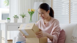Young happy asia people teen girl smile enjoy unbox post mail sit relax at home comfort sofa couch feel joy amazed awe wow in omni channel fast send parcel via online sale shop store e-commerce order.
