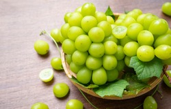 Green grape in Bamboo basket on wooden table in garden, Shine Muscat Grape with leaves in wooden background
