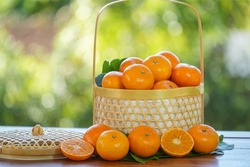 Fresh Tangerine Orange with slices on blurred greenery background, Mandarin Orange fruit in Bamboo basket on wooden table in garden.