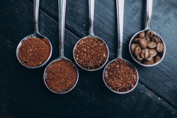 Coffee beans of different degrees of roasting and grinding are scattered in metal spoons. Texture background.