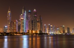 Panoramic night view of Dubai Marina skyscrapers and their reflections in the bay