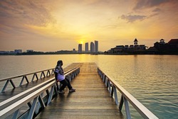A women sitting at Jetty at lakeside while enjoying a colorful Sunrise, Pullman, Putrajaya, Malaysia.