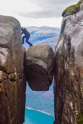 The tourist hiker man leaves from Kjeragbolten - the most dangerous stone in the world. Kjeragbolten is a rock stuck at an altitude of 984 meters above Lysefjorden on mountain Kjerag, Norway.