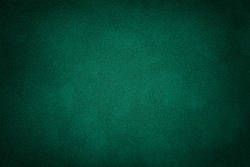 Dark green matte background of suede fabric, closeup. Velvet texture of seamless deep emerald leather. Felt material macro with vignette.