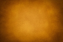 Dark orange matte background of suede fabric with vignette, closeup. Velvet texture of seamless golden textile with gradient, macro. Structure of amber felt canvas backdrop.