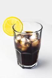 Highball cocktail glass with slice of lemon on the side full of cola with ice isolated on white background. Soft drink in big glass.