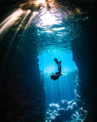 Girl diving in cavern with lightbeams coming on top of her