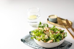 Healthy salad with  different lettuce, croutons,cheese,  chicken and dressing with especial sauce. Caesar salad in the white plate served with glass water and gold cutlery on the restaurant table.