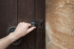 Person seen opening a medieval door at an entrance to a medieval castle in Europe. The rough wooden texture and stone work wall is evident.