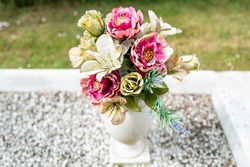 Artificial flowers seen in a porcelain vase located on a grave in a rural cemetery.