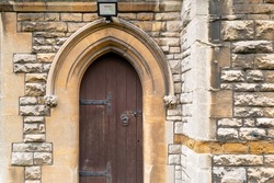 Architectural view of a wooden medieval door leading to a crypt in a very old English church. Note the PIR security light on the arch.