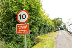 Shallow focus of a 10mph generic speed sign and a generic reduce speed for pedestrians seen down a rural road.