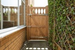 Shallow focus of a newly installed thick wooden gate. Part of a conservatory is seen on the left, a detached garage is on the right.