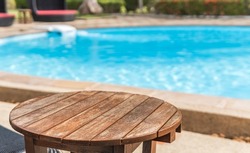 Round wooden table and blurred empty swimming pool on day light