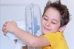 preschool boy cooling in front of fan. Little child refreshing from heat in front of small fan at home. Cute small kid play with ventilator blowing cool wind alone.