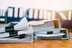 Stack of business report paper file on modern white office desk with bokeh background.