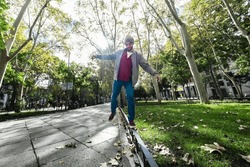Urban elegance: Bearded gentleman showcases stylish balance on a Madrid sidewalk, wide-angle shot.