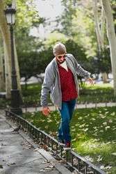 Madrid's street balance: Bearded man, red-checks, poised on a sunlit fence.