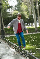 In Madrid's autumn, a bearded man effortlessly balances on a sunlit street fence.