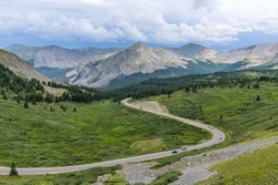Cottonwood Pass - A panoramic Summer day view of a mountain road winding in a green valley at east of  the summit of Cottonwood Pass. Buena Vista - Crested Butte, Colorado, USA.