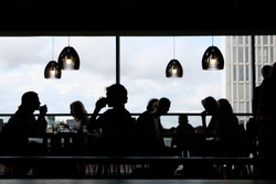 Black silhouettes of people having lunch inside a modern restaurant with big windows