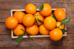 fresh orange fruits with leaves in a box on wooden table, top view