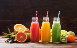 bottles of fruit juice and smoothie with fresh fruits on wooden table