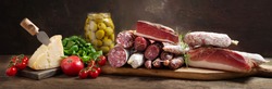 Italian food. Various kind types of salami, speck, sausages, parmesan cheese, green olives, basil and fresh tomatoes on a wooden table